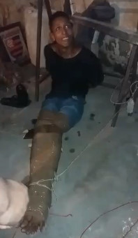 Taped thief is lightly beaten with a stick